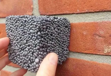 Close-up van een hand die een uitgezaagd stukje muur toont met vastgelijmde EPS-parels, als voorbeeld van de isolatieopvulling in de spouwmuur