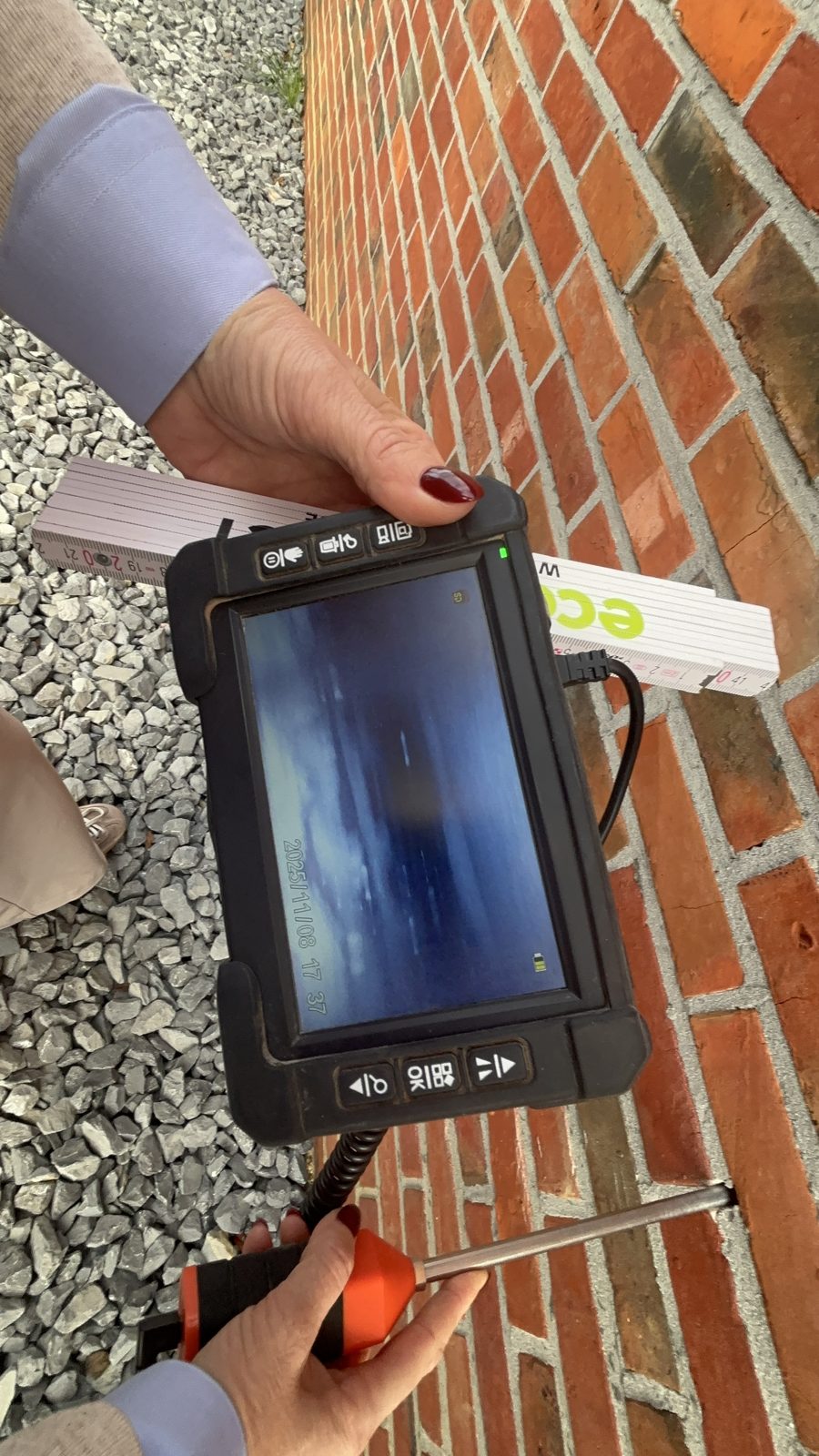 Camera-inspectie van de spouw: een inspecteur van Eco Protect leest het scherm van de endoscoop af terwijl de camera via een gat in de voeg de spouw bekijkt