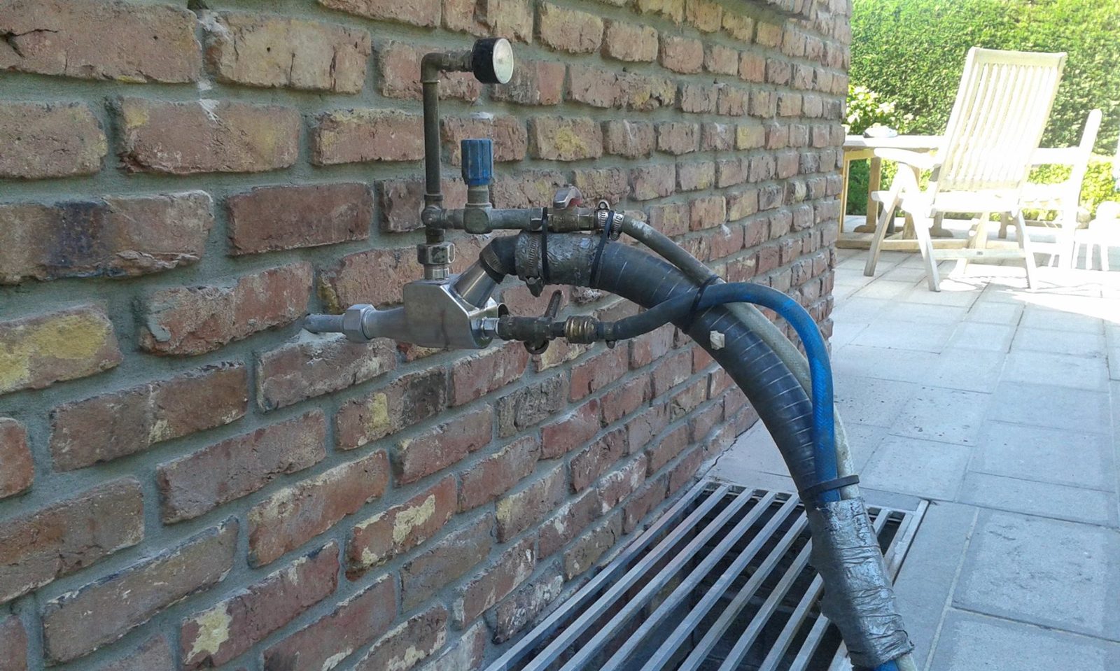 Inblaaspistool van Eco Protect in de voeg van een bakstenen gevel, met de slangen voor de EPS-parels en de lijm UniGlue 2.0